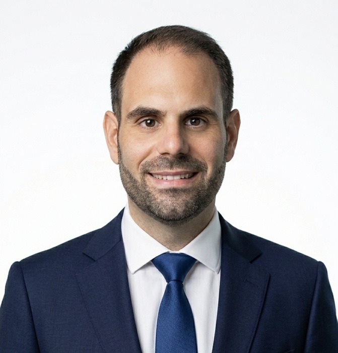 Jose M. Romero, pictured from head to mid chest. He is smiling at the camera. He is wearing a navy suit, deep blue tie and a white button down shirt.